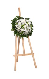 Photo of Funeral wreath of flowers on wooden stand against white background