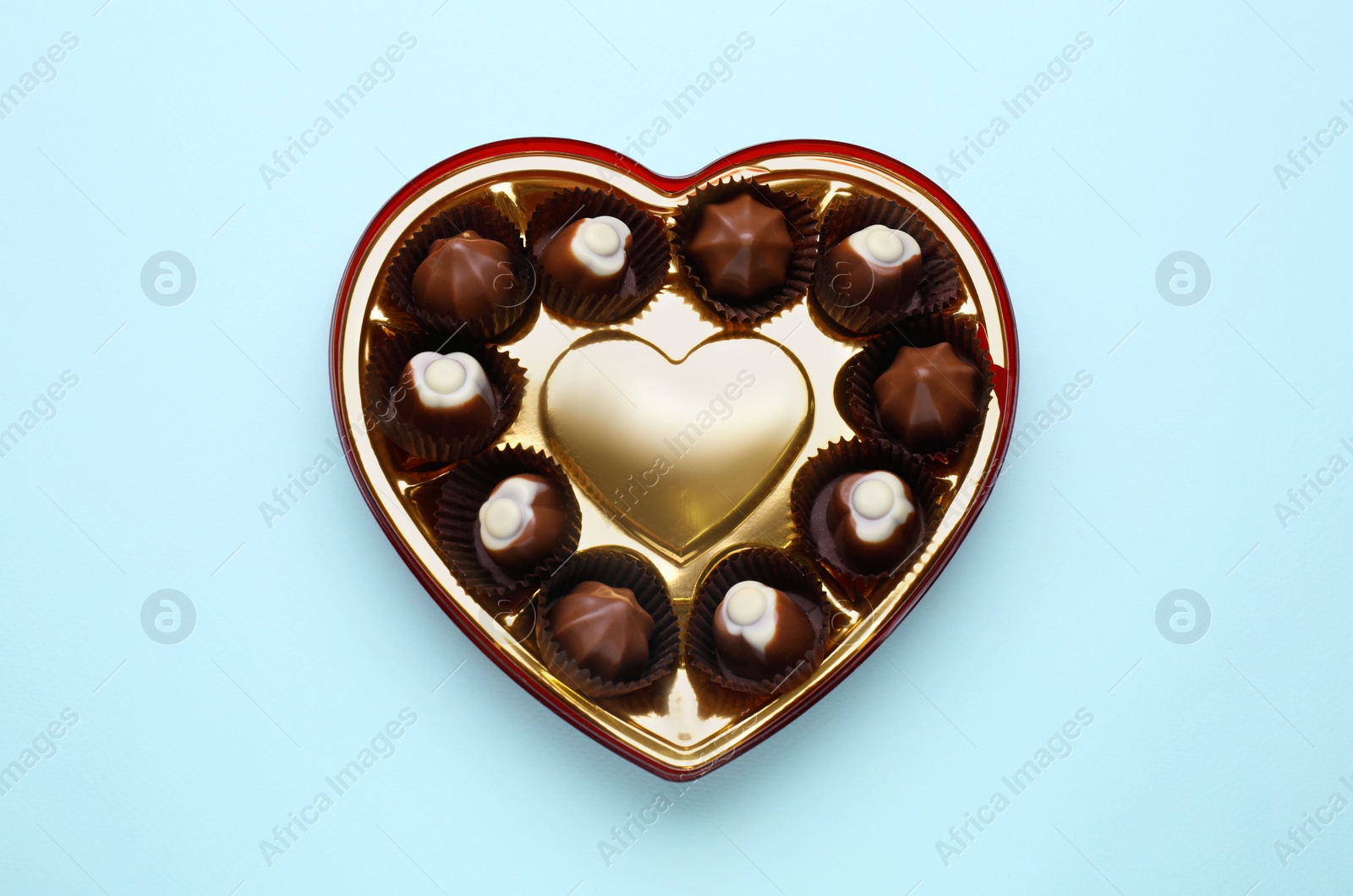 Photo of Heart shaped box with delicious chocolate candies on light blue background, top view