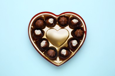 Heart shaped box with delicious chocolate candies on light blue background, top view
