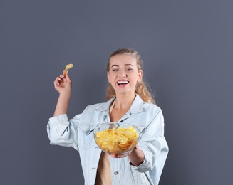 Woman with bowl of potato chips on grey background