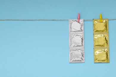 Photo of Clothesline with packaged condoms on light blue background, space for text. Safe sex