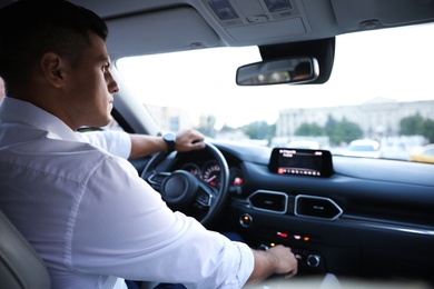 Photo of Handsome man driving his modern luxury car, view from backseat