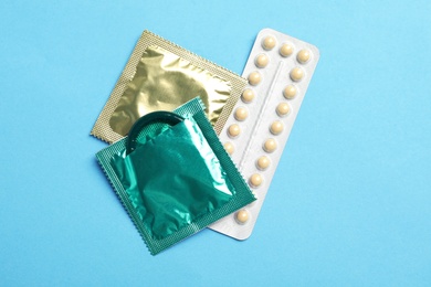 Photo of Condoms and birth control pills on light blue background, flat lay. Safe sex concept
