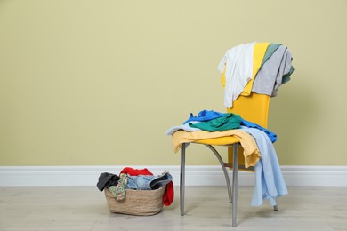 Photo of Yellow chair and wicker basket with different clothes near beige wall, space for text