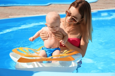 Happy mother with little baby in swimming pool on sunny day