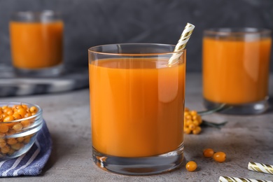 Delicious sea buckthorn juice with straw on grey table, closeup