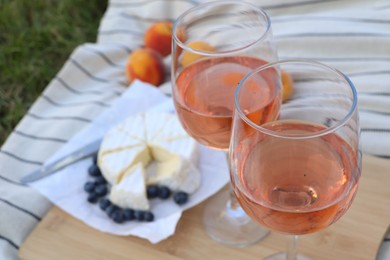 Photo of Glasses of delicious rose wine and food on picnic blanket outdoors, closeup