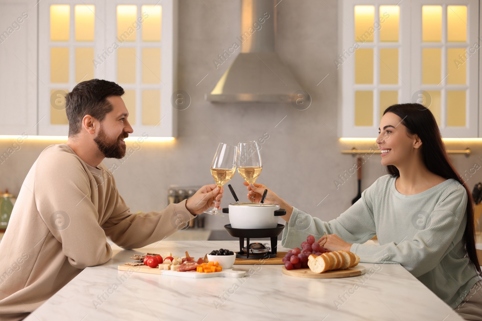 Photo of Romantic date with fondue. Couple clinking glasses of wine at home