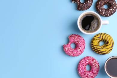 Tasty donuts and cups of coffee on light blue background, flat lay. Space for text