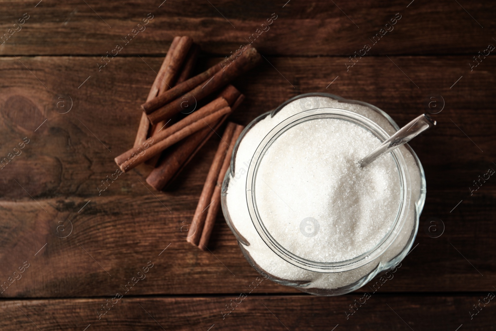 Photo of Glass bowl with sugar and cinnamon on wooden table, flat lay