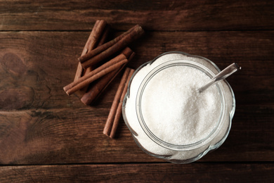 Photo of Glass bowl with sugar and cinnamon on wooden table, flat lay