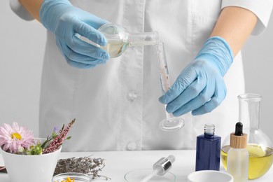 Scientist developing cosmetic oil at white table, closeup