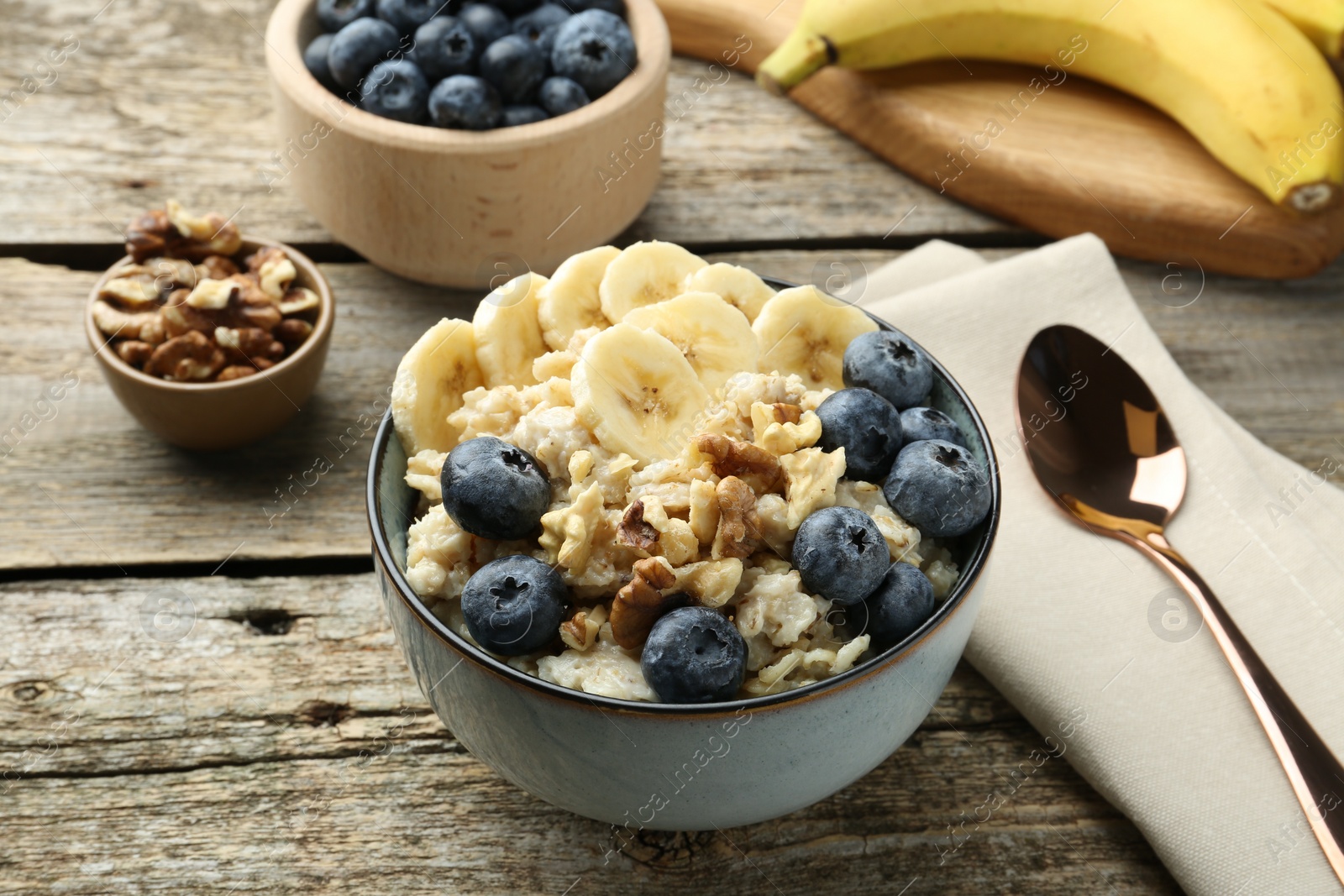 Photo of Tasty oatmeal with banana, blueberries and walnuts served in bowl on wooden table