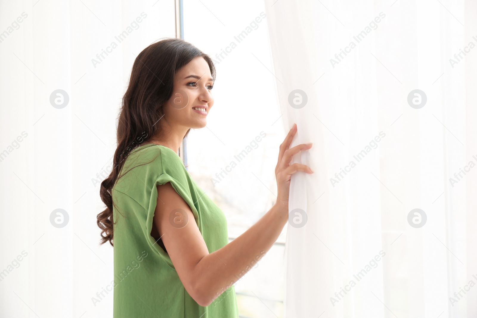 Photo of Beautiful young woman looking out of window at home