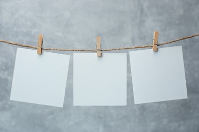 Photo of Wooden clothespins with blank notepapers on twine against grey background. Space for text
