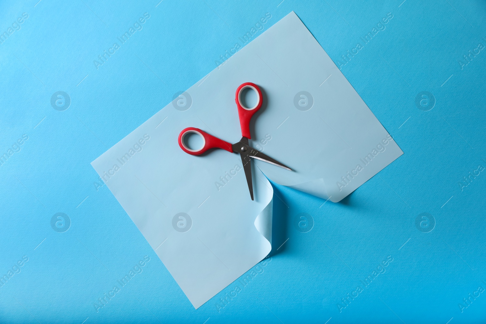 Photo of Red scissors and color paper on light blue background, top view