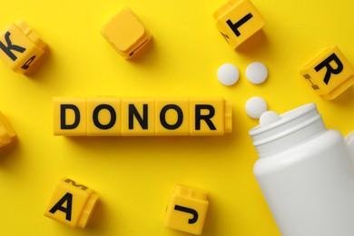 Word Donor made of cubes and pills on yellow background, flat lay