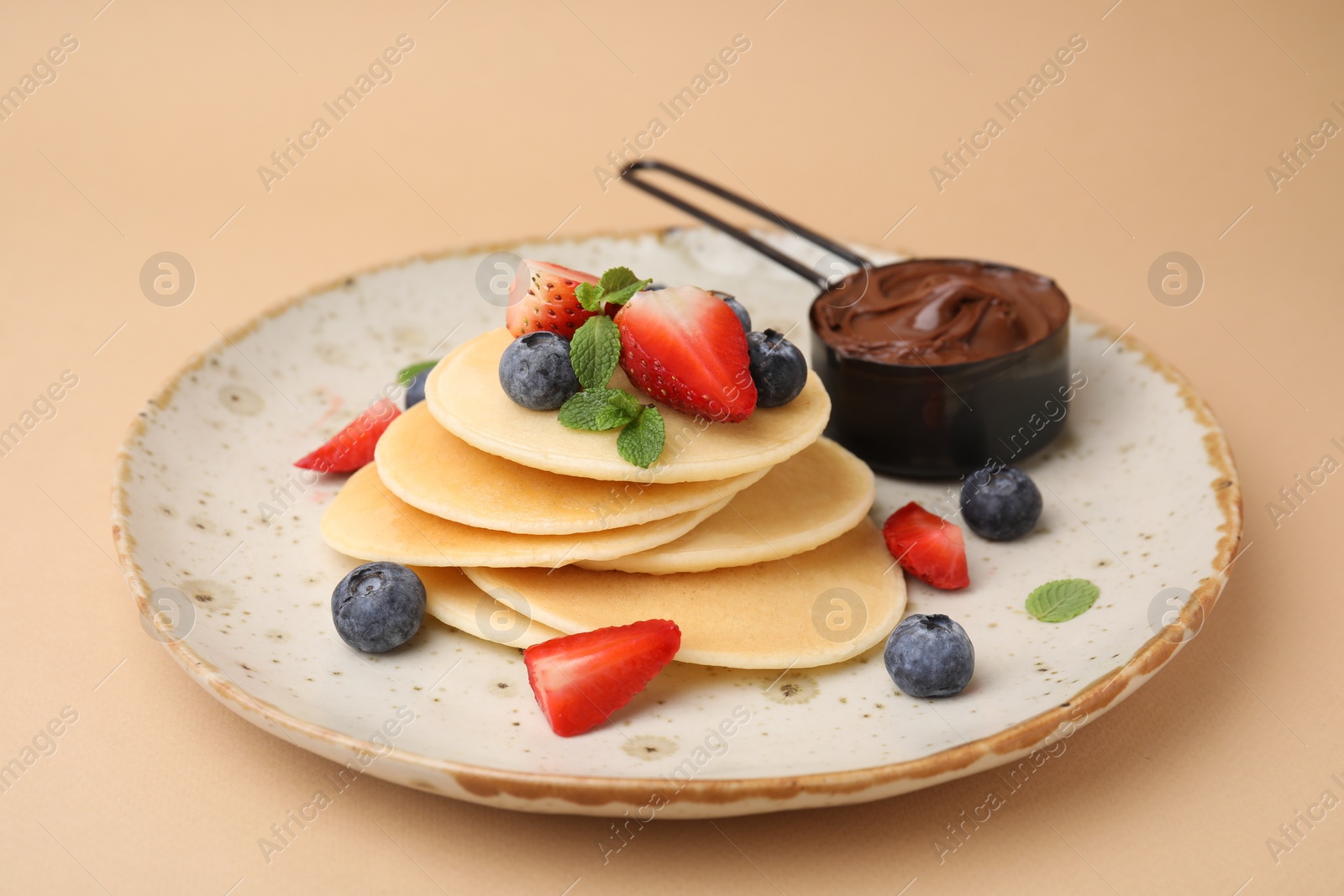 Photo of Delicious pancakes served with berries and chocolate spread on beige background, closeup