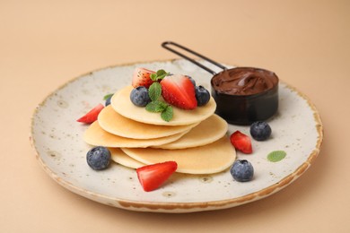 Photo of Delicious pancakes served with berries and chocolate spread on beige background, closeup