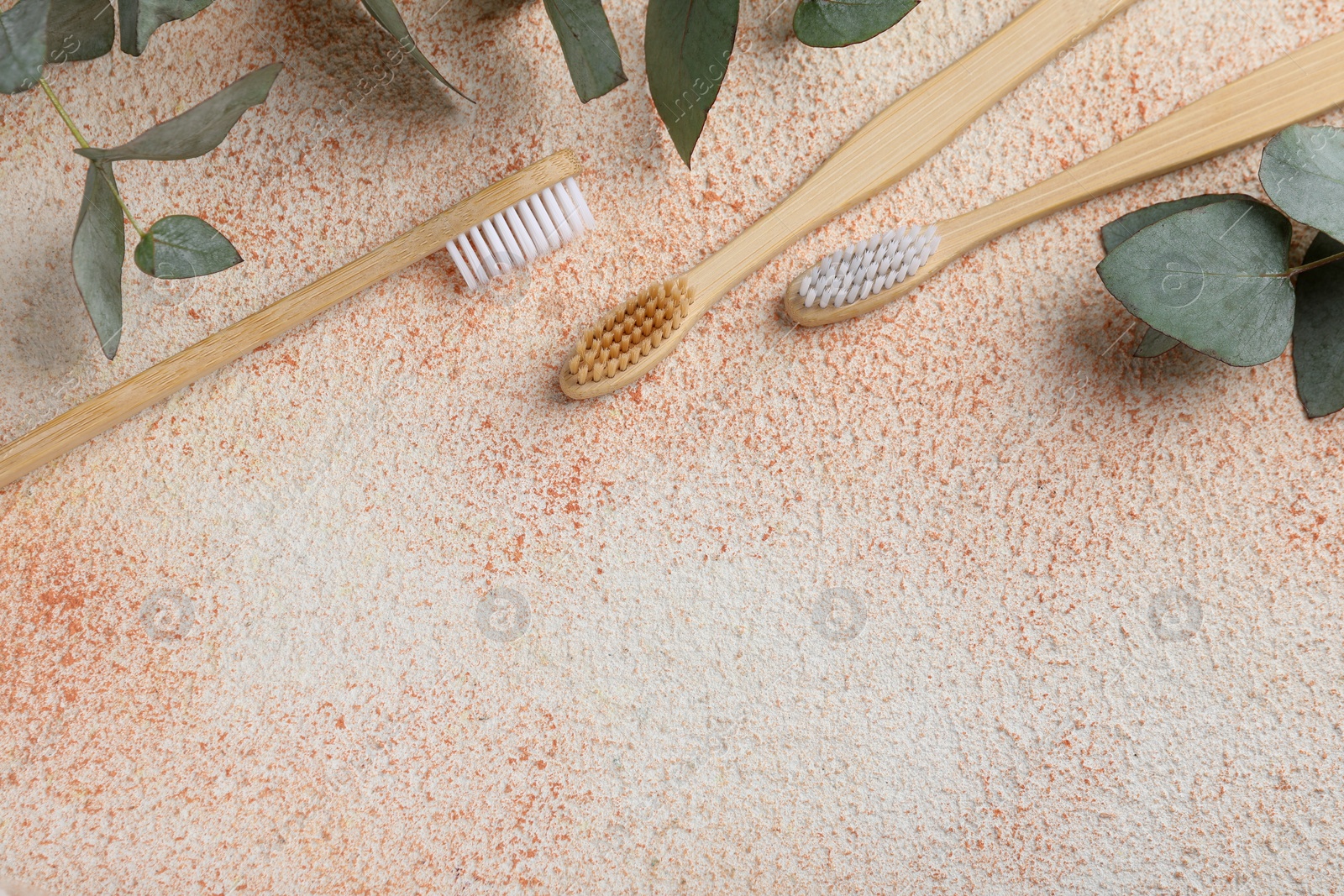 Photo of Bamboo toothbrushes and eucalyptus leaves on beige textured table, flat lay. Space for text