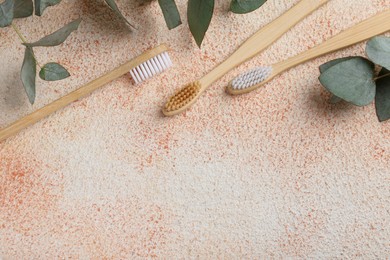 Photo of Bamboo toothbrushes and eucalyptus leaves on beige textured table, flat lay. Space for text