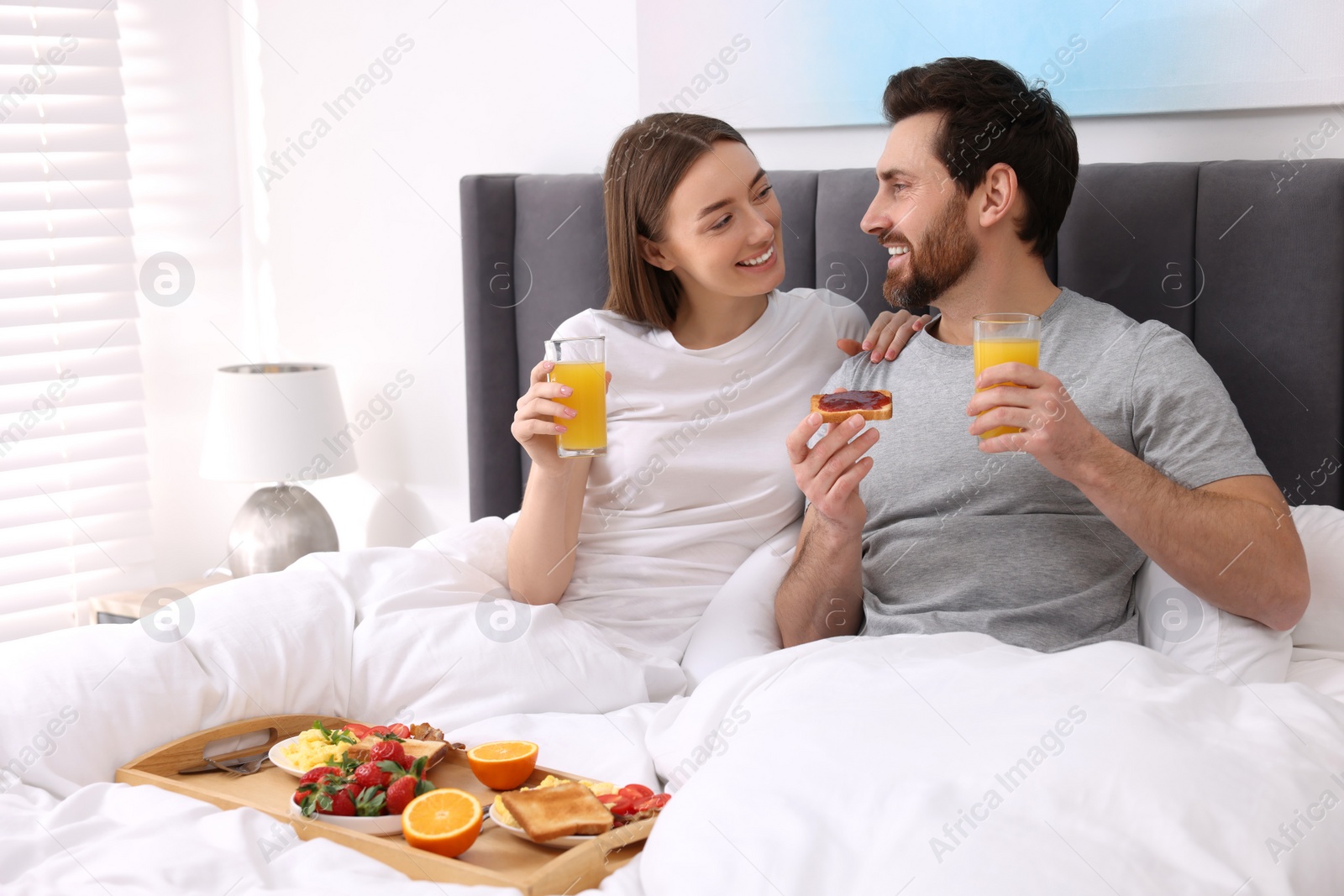 Photo of Happy couple eating tasty breakfast in bed at home