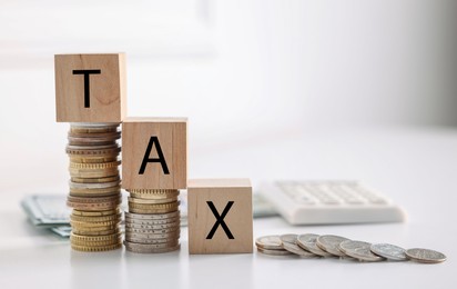Photo of Word Tax made of wooden cubes, coins and calculator on white table