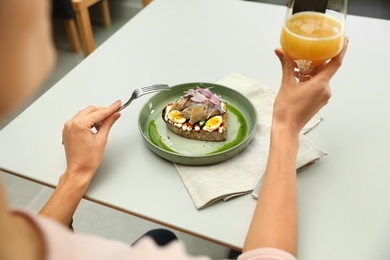 Woman with glass of beer and tasty fish sandwich at light table, closeup