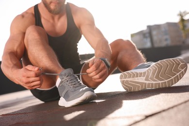 Photo of Man tying shoelaces before running outdoors on sunny day, closeup