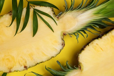 Photo of Halves of ripe pineapple and green leaves on yellow background, flat lay