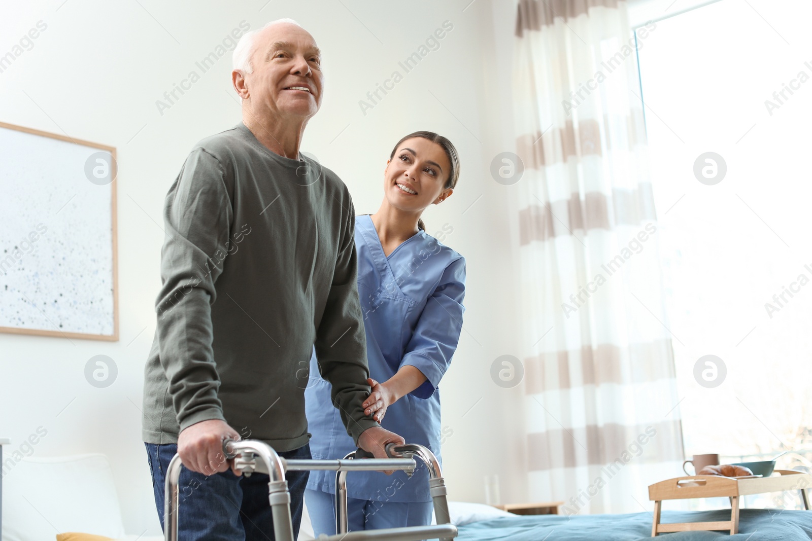 Photo of Care worker helping elderly man with walker in geriatric hospice