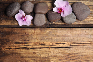 Stones with orchid flowers and space for text on wooden background, flat lay. Zen lifestyle