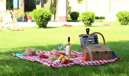 Picnic basket with products and bottle of wine on checkered blanket in garden. Space for text