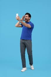 Photo of Emotional man taking selfie with smartphone on light blue background