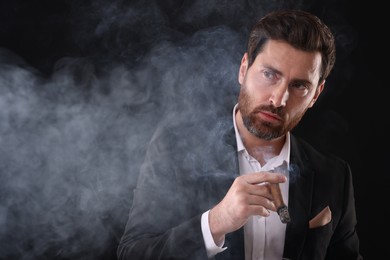 Photo of Handsome man in elegant suit smoking cigar on black background. Space for text