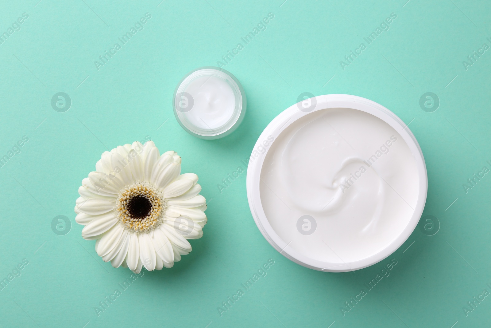 Photo of Moisturizing cream in open jars and gerbera flower on turquoise background, flat lay. Body care products