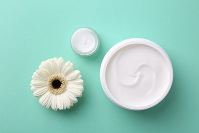 Moisturizing cream in open jars and gerbera flower on turquoise background, flat lay. Body care products