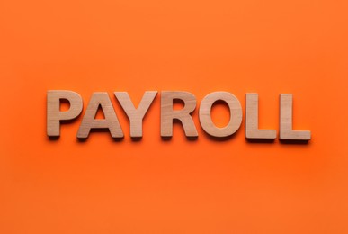 Word Payroll made of wooden letters on orange background, top view