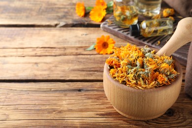 Mortar of dry calendula flowers on wooden table. Space for text