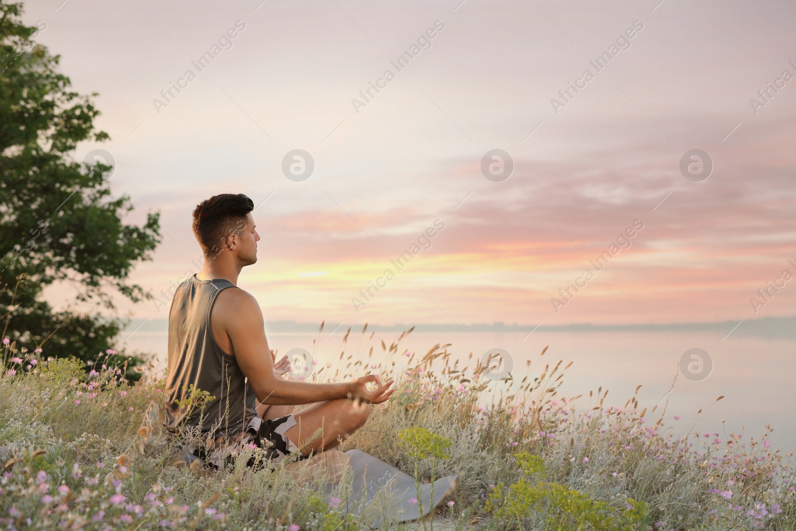 Photo of Man meditating in meadow near river. Space for text