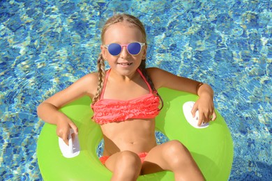 Photo of Cute little girl with sunglasses and inflatable ring in pool on sunny day