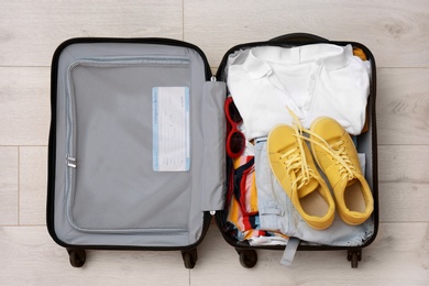 Packed suitcase with clothes and sneakers on wooden background, top view