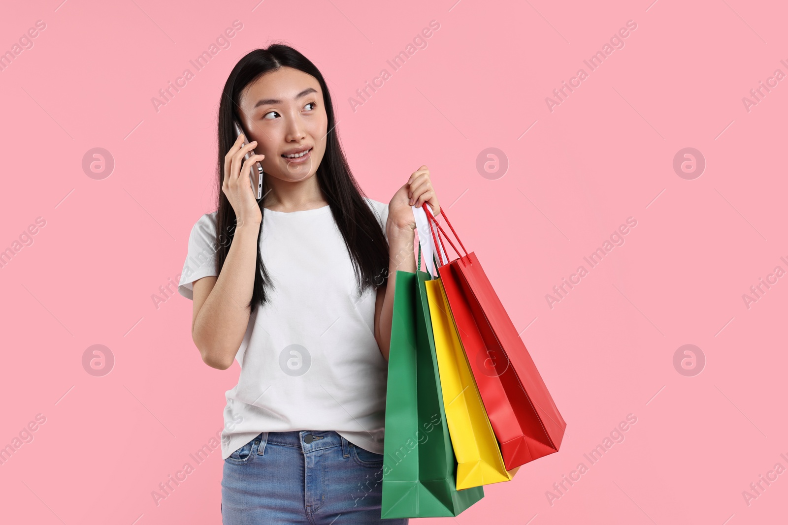 Photo of Smiling woman with shopping bags talking by smartphone on pink background. Space for text