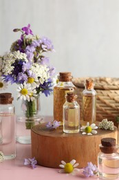 Photo of Aromatherapy. Different essential oils and flowers on pink wooden table