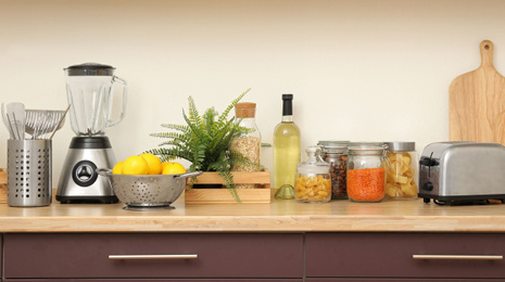 Wooden countertop with appliances and products near white wall. Kitchen interior idea