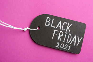 Photo of Tag with words BLACK FRIDAY 2021 on violet background, top view