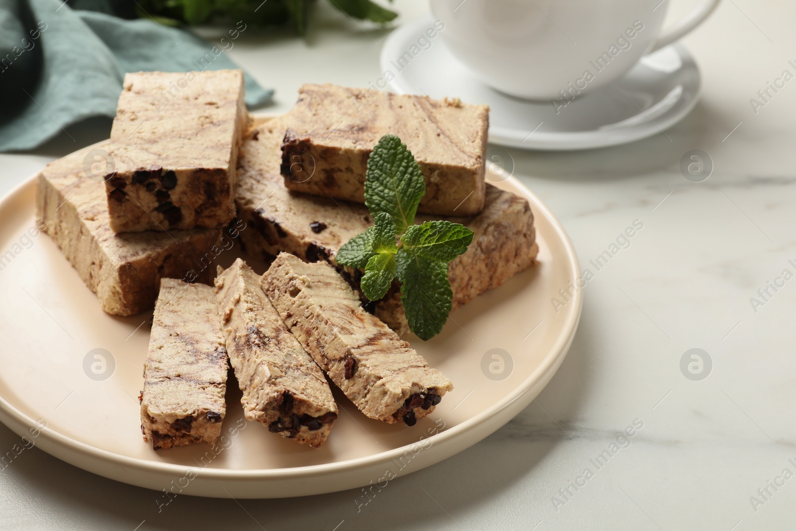 Photo of Pieces of tasty chocolate halva and mint on white marble table, closeup. Space for text