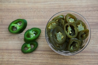 Photo of Fresh and pickled green jalapeno peppers on wooden table, flat lay