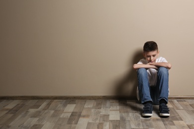 Upset boy sitting on floor at color wall. Space for text