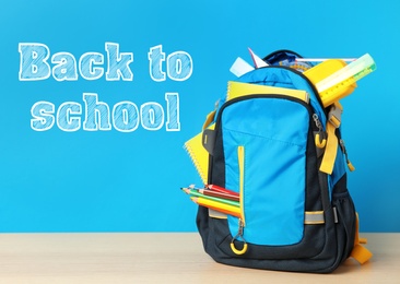 Wooden table with backpack and stationery near text Back To School on blue background